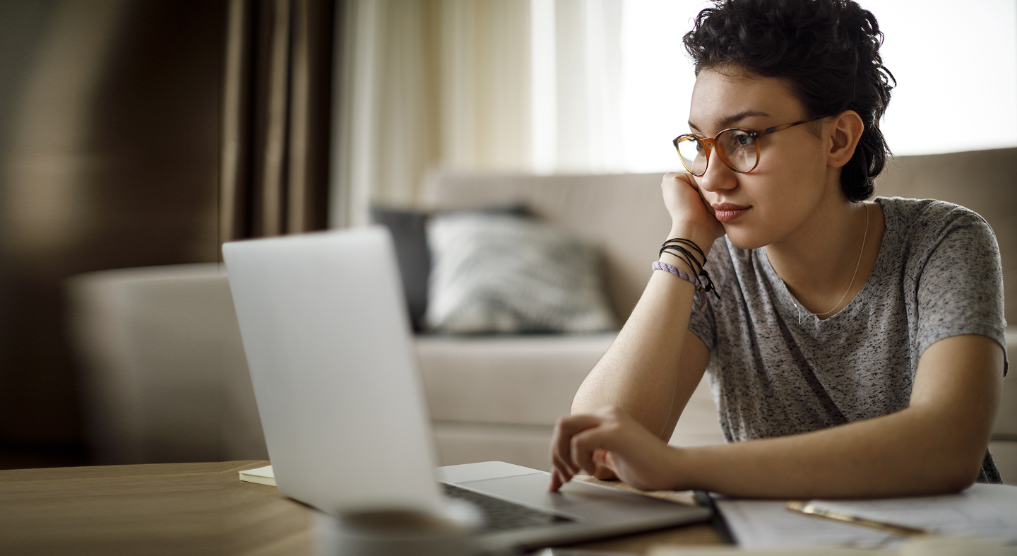 A Girl in her 30s wearing glasses reading on her laptop
